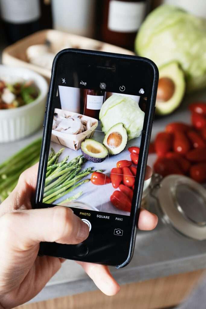 Anonymous crop person taking photo of food on table in kitchen